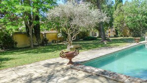 Une piscine dont le bord est revêtu de pierres, entourée d’une pelouse bien entretenue et d’arbres.