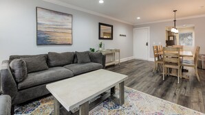 A modern living room with a gray sofa, a wooden dining table with chairs, and a large painting on the wall.