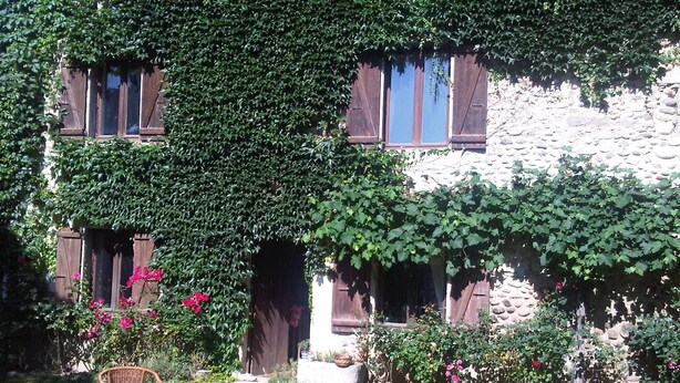 Ein Steingebäude mit efeuüberwucherten Fenstern und einem Garten mit Tisch und Stühlen.
