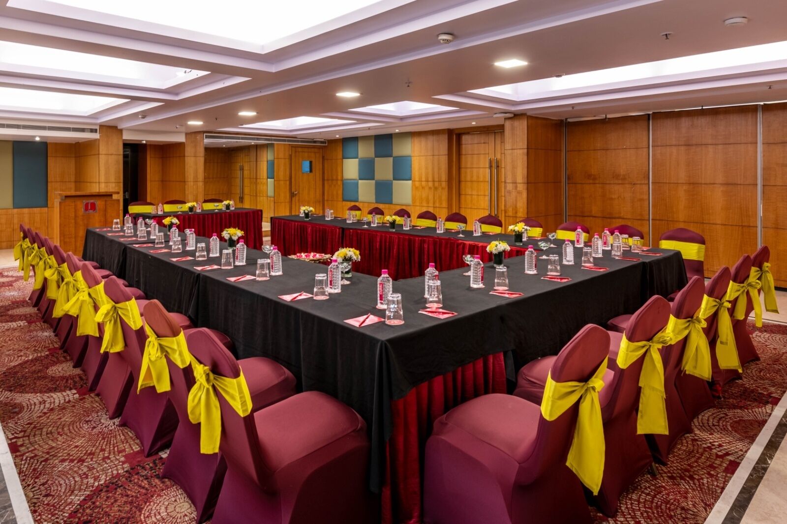 A conference room with a long table, chairs with yellow sashes, and a red carpet.