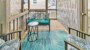 Une véranda couverte avec un banc en bois, une petite table ronde et un tapis à motifs.