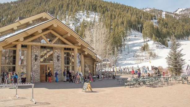 Un chalet à la façade en pierre et aux grandes fenêtres, niché au cœur d’un paysage montagneux enneigé.