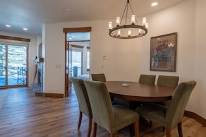 A dining area with a round table and six chairs, a chandelier, and a poster on the wall. - Westridge Condo 26 -Updated Condo w/ AC, Walk to River Run Lifts and Downtown (Ketchum)
