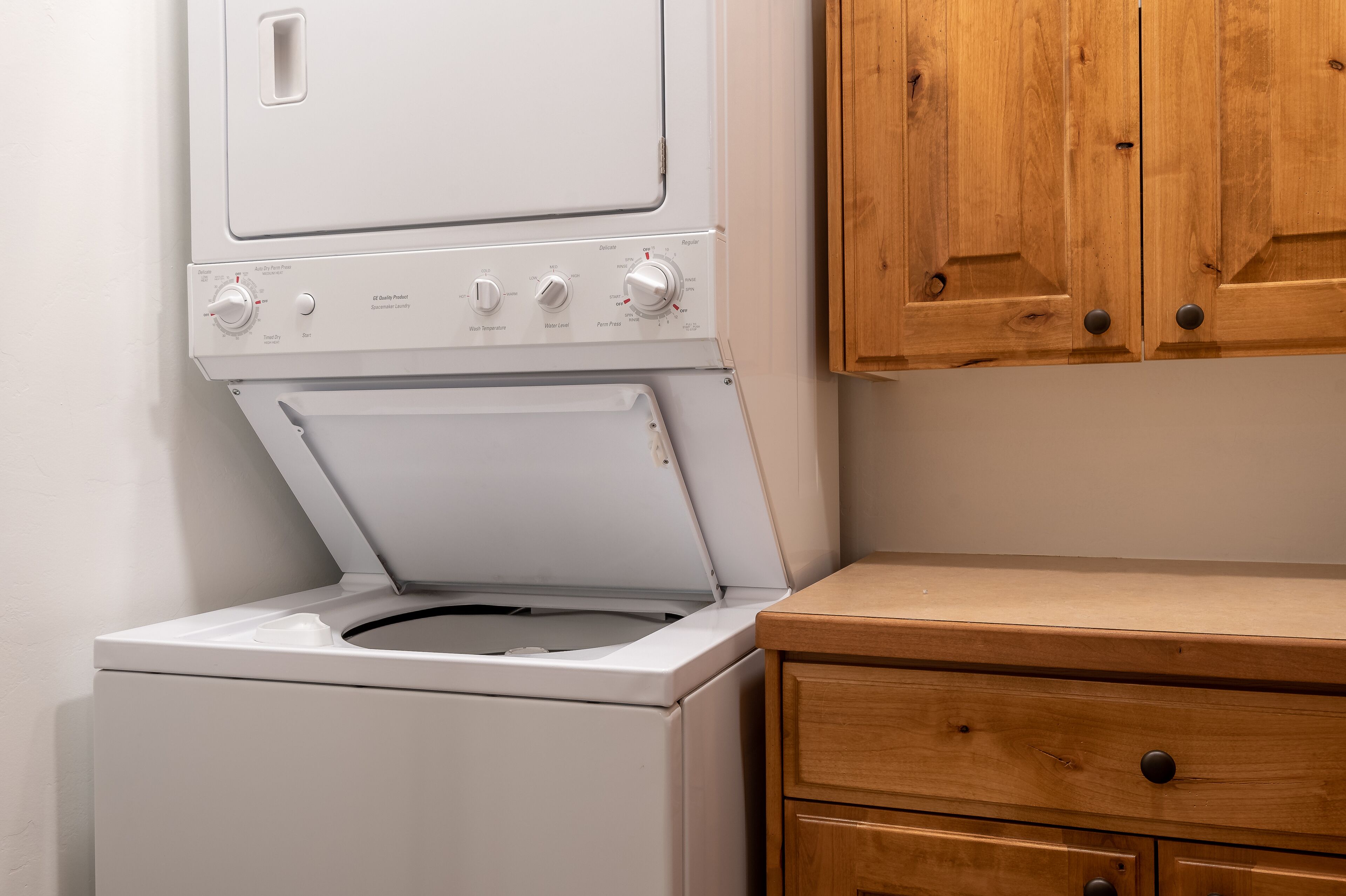 A front-loading washing machine with a wooden cabinet and a drawer unit.
