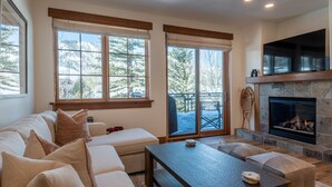 Un salon chaleureux avec une cheminée en pierre, de grandes fenêtres et un coin salon confortable.
