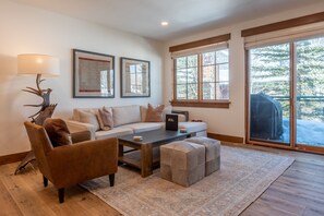 A modern living room with a sofa, coffee table, and ottoman, a deer antler lamp, and framed documents on the wall. - Westridge Condo 26 -Updated Condo w/ AC, Walk to River Run Lifts and Downtown (Ketchum)