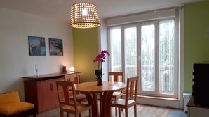 A dining area with a wooden table and chairs, a potted plant, and a hanging light fixture. - Agréable Appartement Dans Résidence Avec Jardin Très Proche des Commodités (Pont-l'Abbé)