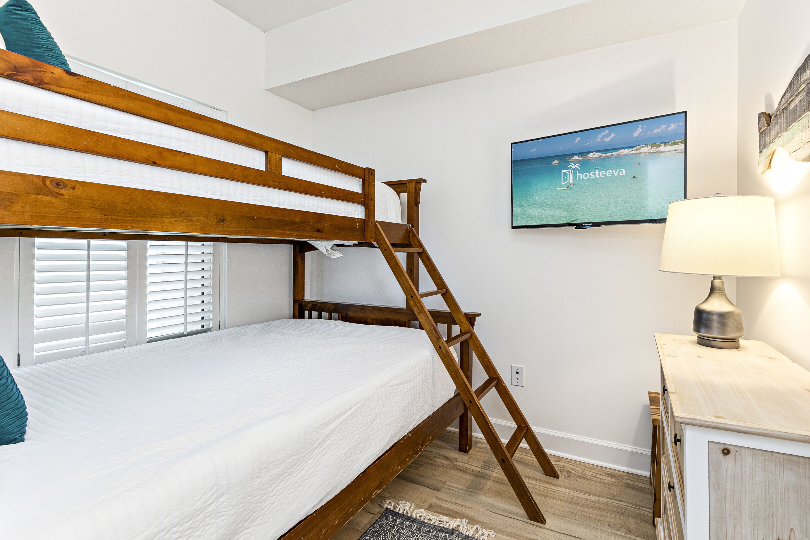 Un lit superposé avec une échelle en bois, un téléviseur fixé au mur et une lampe sur une table de chevet.