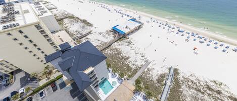 A beach resort with a swimming pool, beach umbrellas, and a pier in the background.