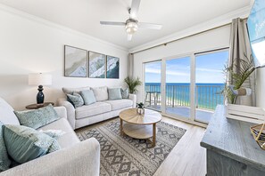 A spacious living room with a large window, a ceiling fan, a sofa, a coffee table, and a view of the ocean. - Seawind 1601 (Gulf Shores)