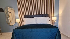 A neatly made bed with a dark blue bedspread, two bedside lamps, a large mirror, and a striped headboard. - Art Flat Municipio (Naples)