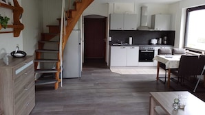 A modern kitchen with a wooden staircase, a dining area with a table and chairs, and a view of the outside through a large window. - Vacation apartment with dog in Cuxhaven Sahlenburg Apartment 3 (Cuxhaven)
