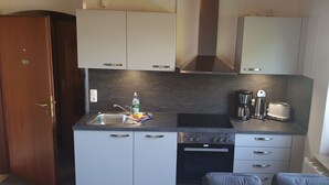 A compact kitchen with white cabinets, a black countertop, a built-in dishwasher, and a window providing natural light. - Vacation apartment with dog in Cuxhaven Sahlenburg Apartment 3 (Cuxhaven)