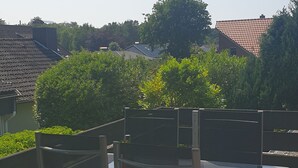 An outdoor seating area with two chairs and a table, an umbrella, and a view of buildings and trees in the background. - Vacation apartment with dog in Cuxhaven Sahlenburg Apartment 3 (Cuxhaven)