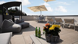 Une terrasse sur le toit aménagée avec un canapé, des chaises, une table avec des bouteilles et un arrangement floral.