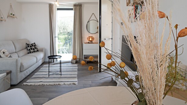 Un salon moderne avec un canapé, une table basse et un téléviseur. Il y a un balcon avec vue sur la verdure.