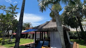 A tropical resort with palm trees, a thatched-roof hut, and outdoor seating. - Hotel Casa Paradiso (Guarujá)