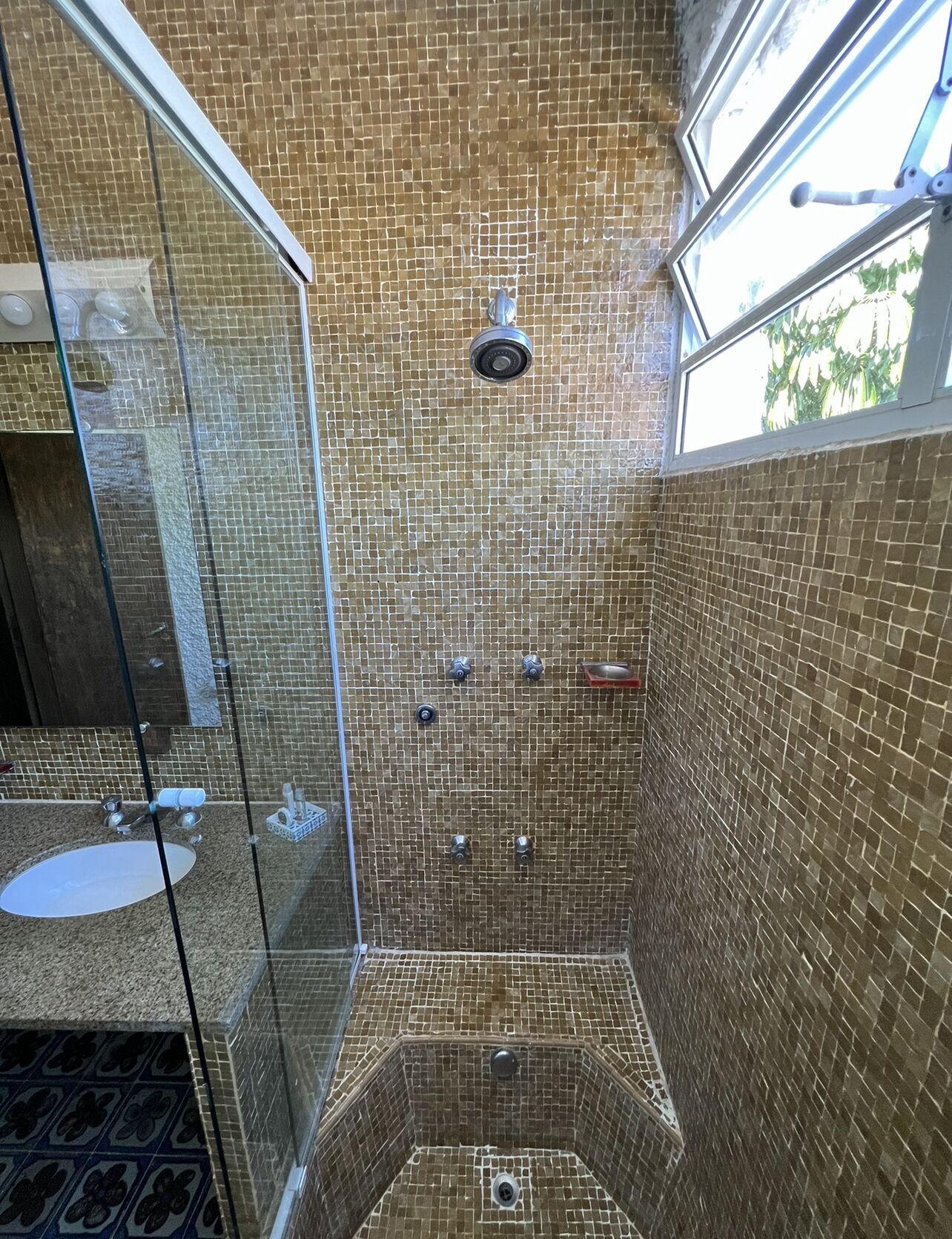 A bathroom with a glass shower enclosure, a sink, and a tiled wall.