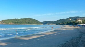 A beach with clear blue water, sandy shore, and hills in the background. - Hotel Casa Paradiso (Guarujá)