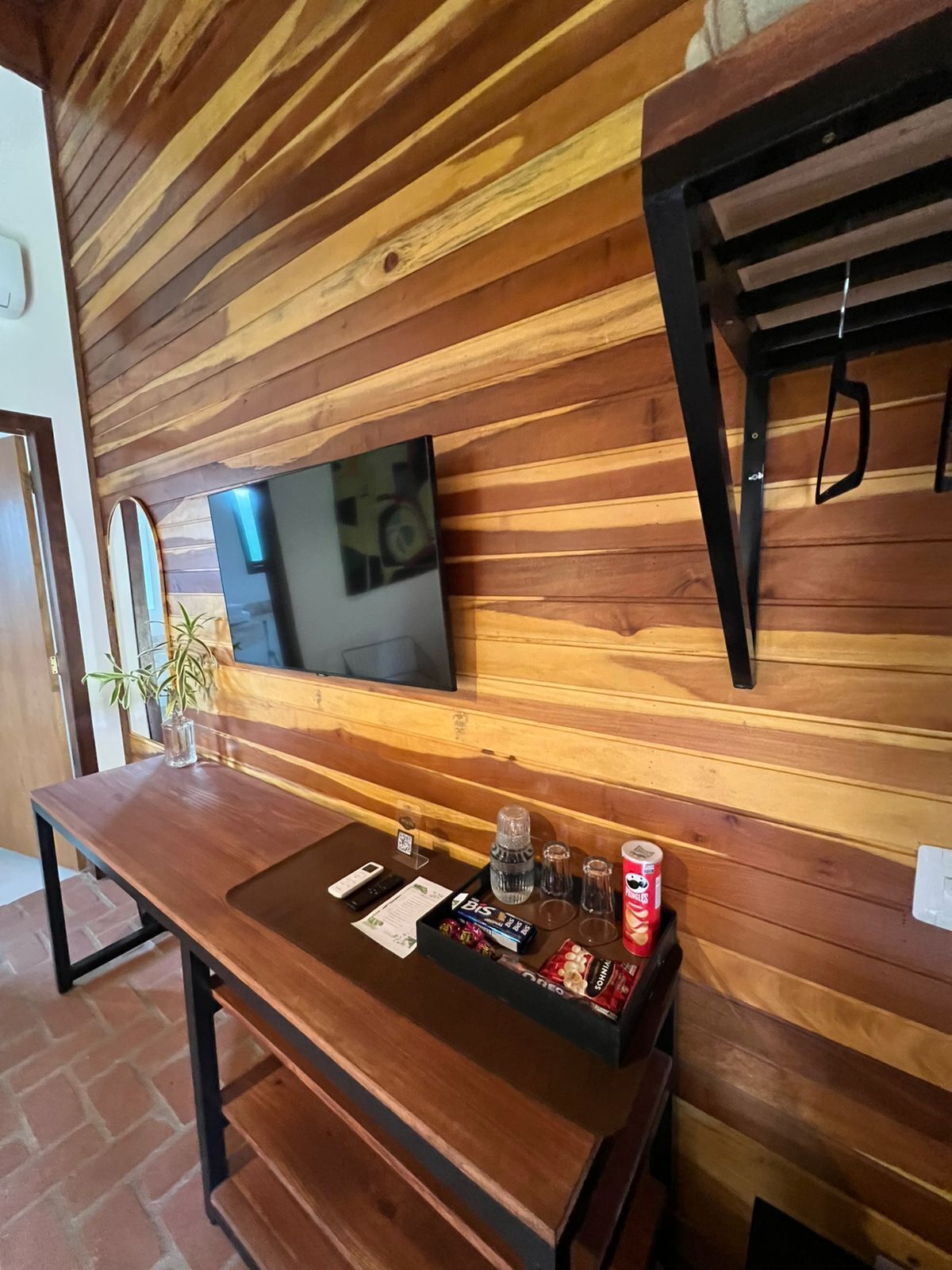A wooden wall with a flat-screen TV mounted above a wooden table with a tray of snacks and condiments.