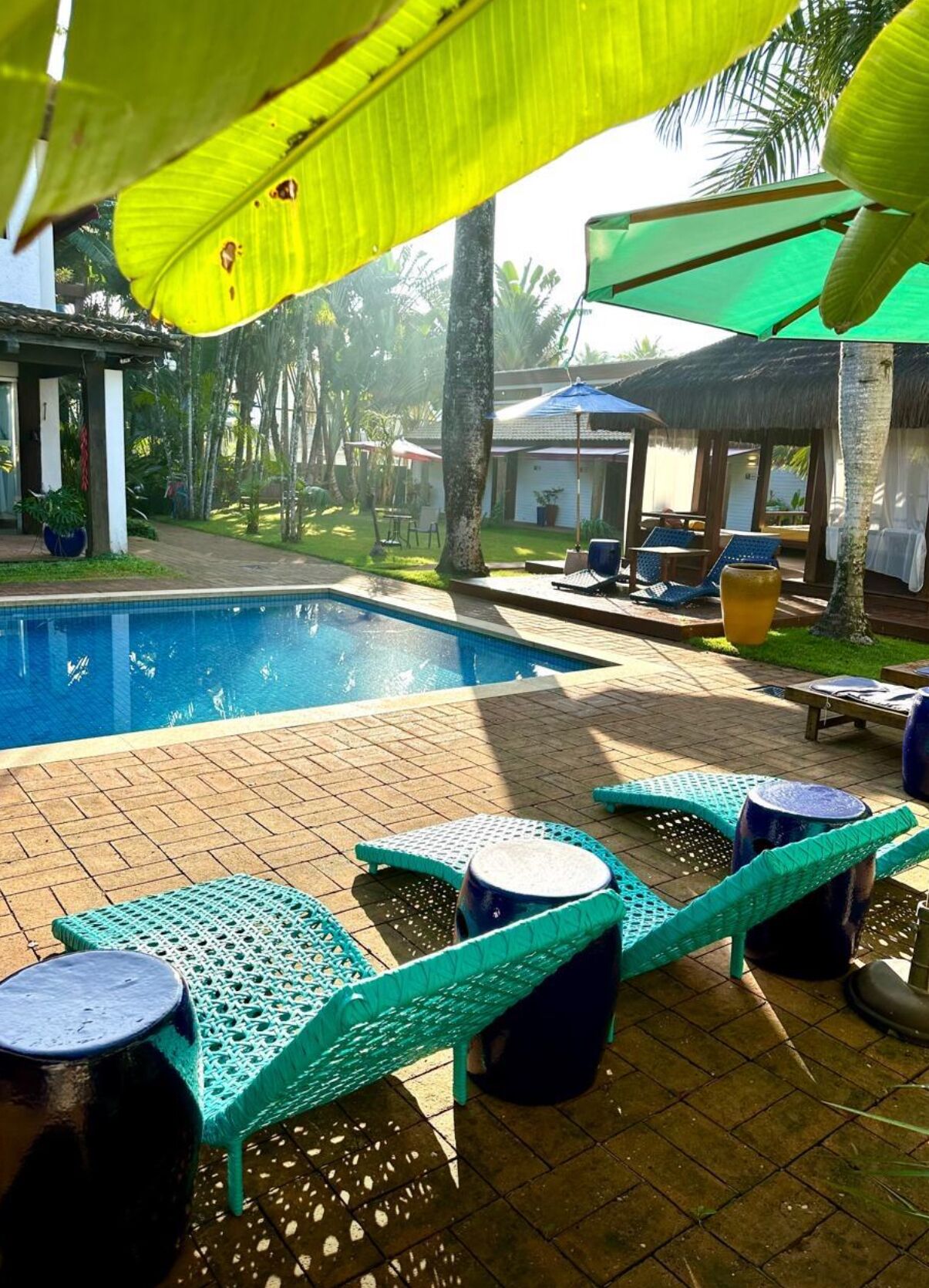 A pool area with lounge chairs and umbrellas, surrounded by greenery.