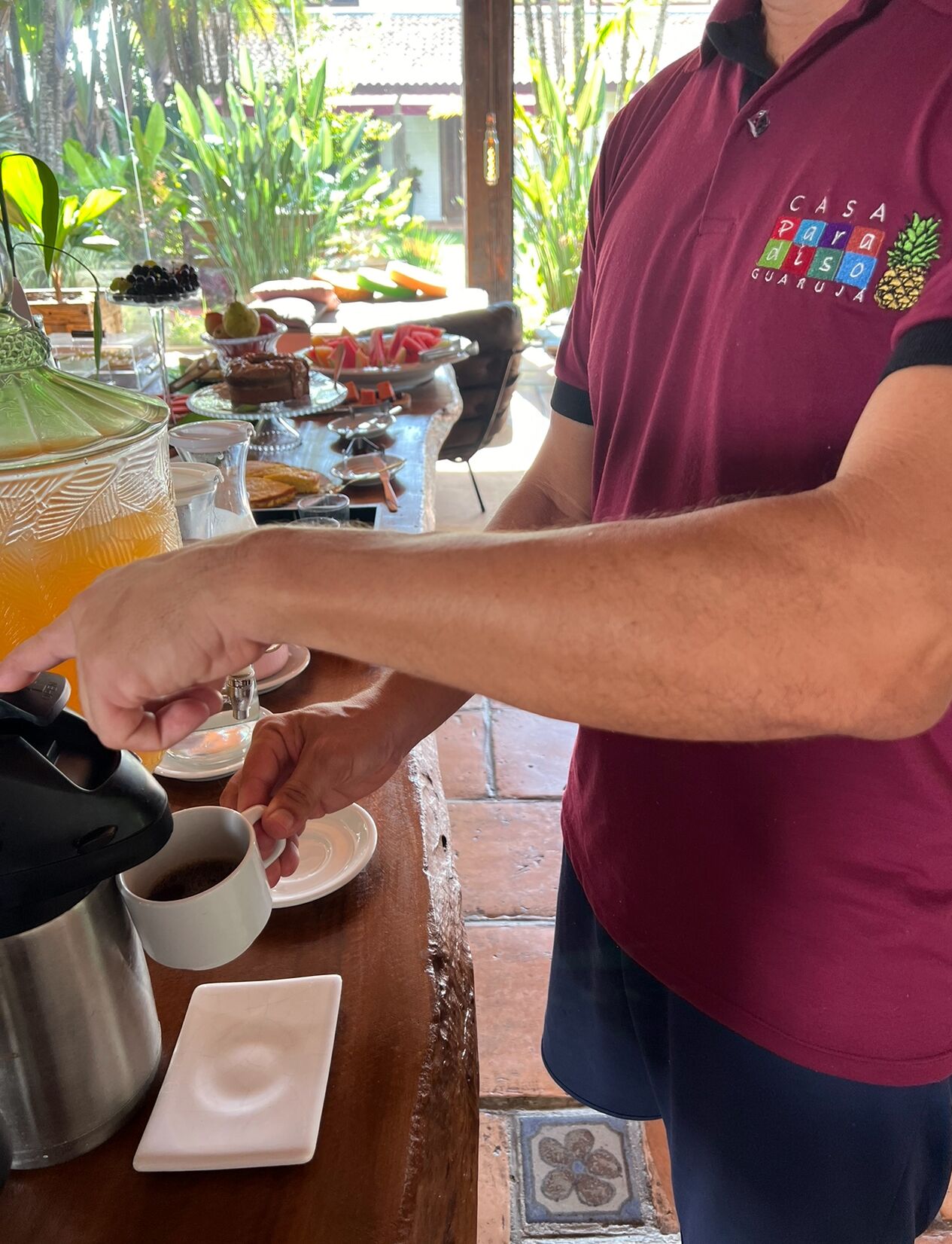 A person pouring coffee into a cup at a table with various food items and a glass of orange juice.