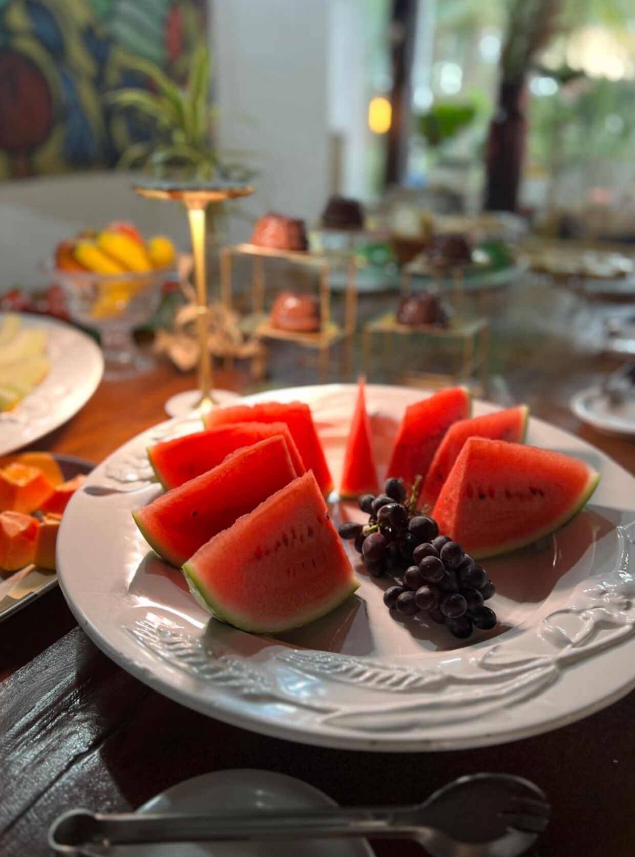 Un plato de rebanadas de sandía y uvas sobre una mesa con un centro de mesa decorativo y un cuadro de fondo.