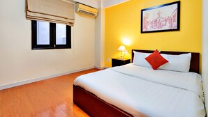 A hotel room with a bed, a nightstand with a lamp, a window with a blind, and an air conditioning unit. - HANZ 4013 Hotel Saigon (Ho Chi Minh City)