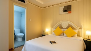 A hotel room with a bed, bedside lamps, a nightstand, a book, and a bathroom with a toilet and shower. - HANZ 4013 Hotel Saigon (Ho Chi Minh City)