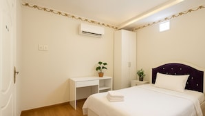 A bedroom with a bed, a desk, a wardrobe, an air conditioner, and a potted plant. - HANZ 4013 Hotel Saigon (Ho Chi Minh City)