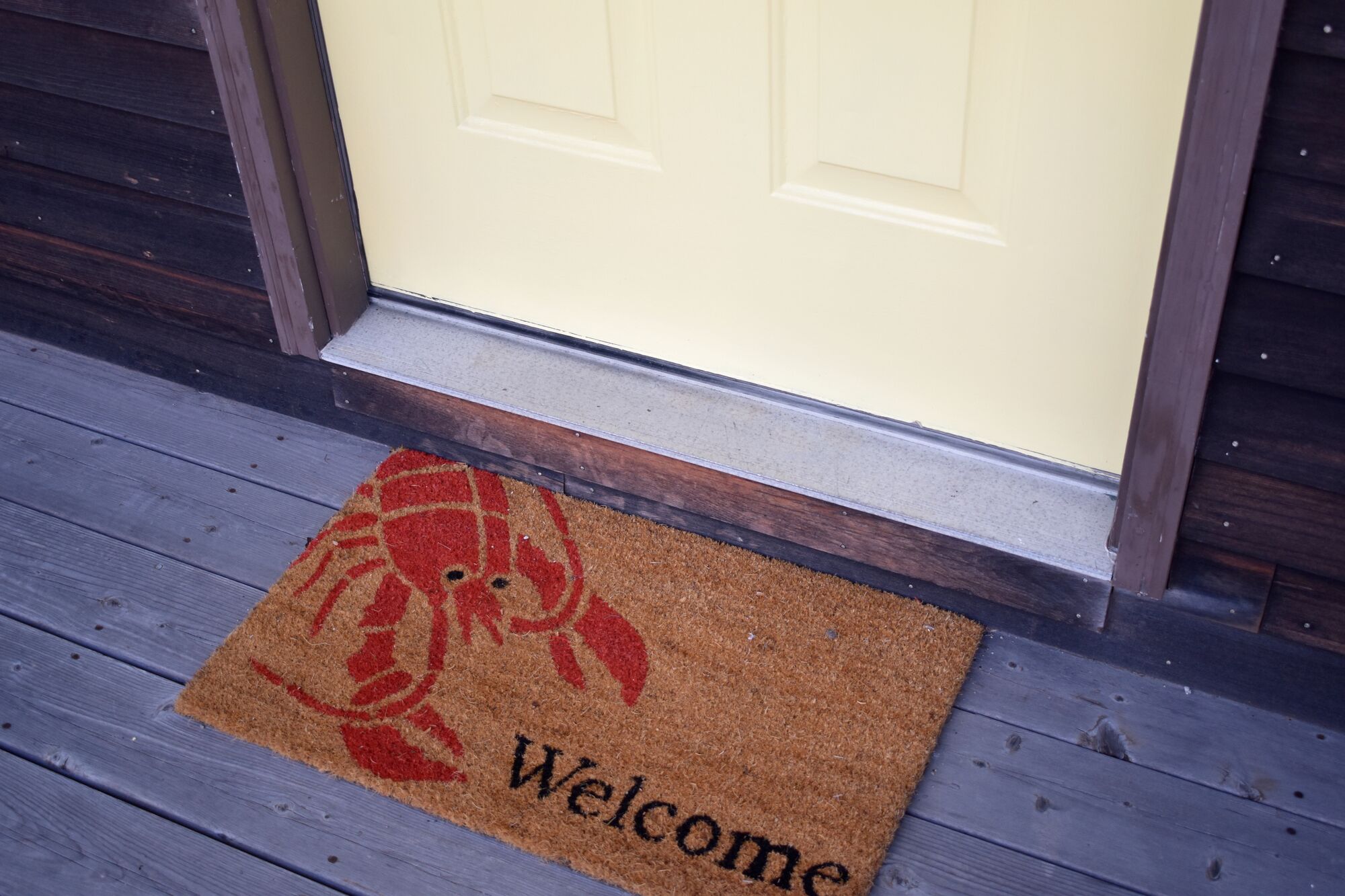 A welcome mat with a crab design and the word "Welcome" on a wooden porch.