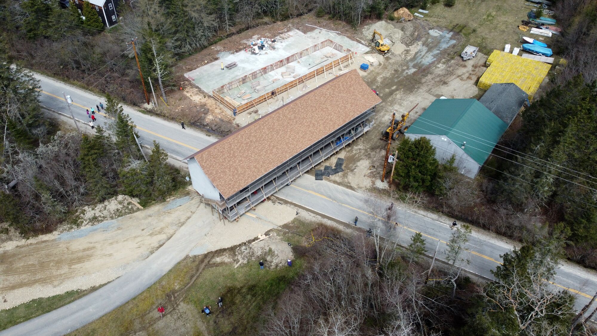 An aerial view of a building under construction with a long, rectangular structure and a sloped roof.