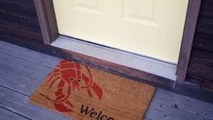 Kynäkuviolla koristeltu tervetulomatto, jossa on sana ”Welcome”, ja se on sijoitettu puisen kuistin eteen.