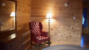 Ein Zimmer mit Holzwänden, einem roten Ledersessel, einem Schmuckkästchen und einer Stehlampe.