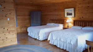 Ein Holzhütten-Zimmer mit zwei Betten, einem Kleiderschrank, einem gerahmten Bild an der Wand und einer Lampe auf dem Nachttisch.
