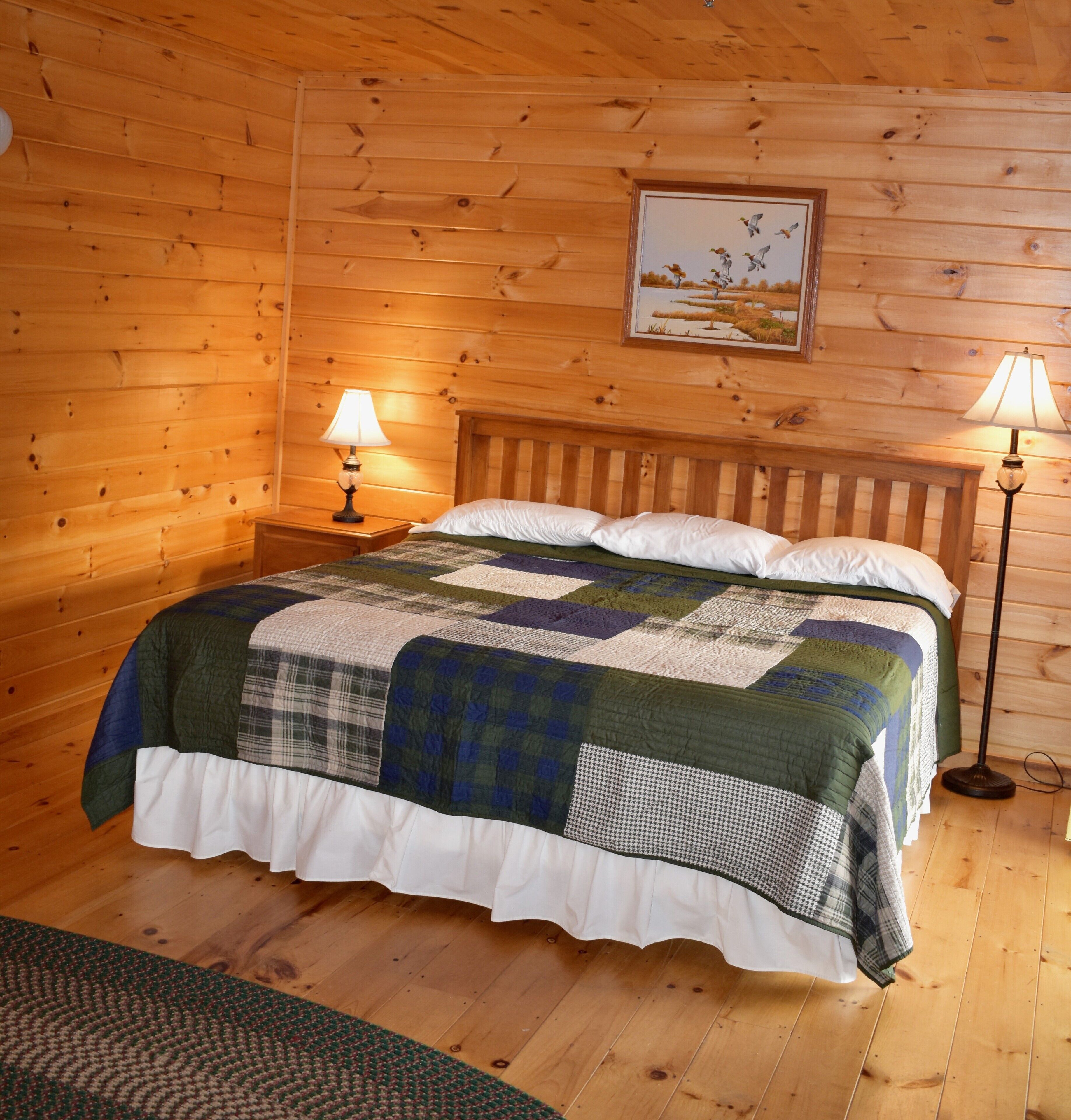 Une chambre dans une cabane en bois, avec un lit, deux lampes de chevet, un tableau au mur et un plancher en bois.