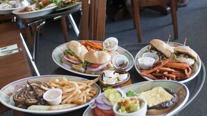 Un restaurant avec plusieurs tables et chaises, proposant différents plats, notamment des hamburgers, des frites et des salades, et où l'on peut voir des clients en train de déjeuner ou de dîner.