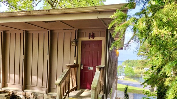 A wooden building with a red door, a stone staircase, and a view of a lake. - Lake View Queen Guest Room With Two Queens, Sleeper Sofa And Patio Overlooking Lake Ouachita. 1 Bedroom Hotel Room by RedAwning (Mount Ida)