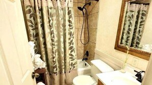 A bathroom with a toilet, sink, shower, and a mirror. - Lake View Queen Guest Room With Two Queens, Sleeper Sofa And Patio Overlooking Lake Ouachita. 1 Bedroom Hotel Room by RedAwning (Mount Ida)