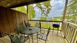 A covered outdoor deck with a round table and chairs, a grill, and a view of a body of water. - Lake View Queen Guest Room With Two Queens, Sleeper Sofa And Patio Overlooking Lake Ouachita. 1 Bedroom Hotel Room by RedAwning (Mount Ida)