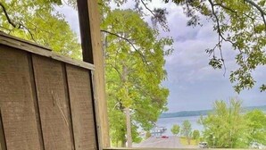 A wooden rocking chair on a porch with a view of a road and trees. - Lake View Queen Guest Room With Two Queens, Sleeper Sofa And Patio Overlooking Lake Ouachita. 1 Bedroom Hotel Room by RedAwning (Mount Ida)