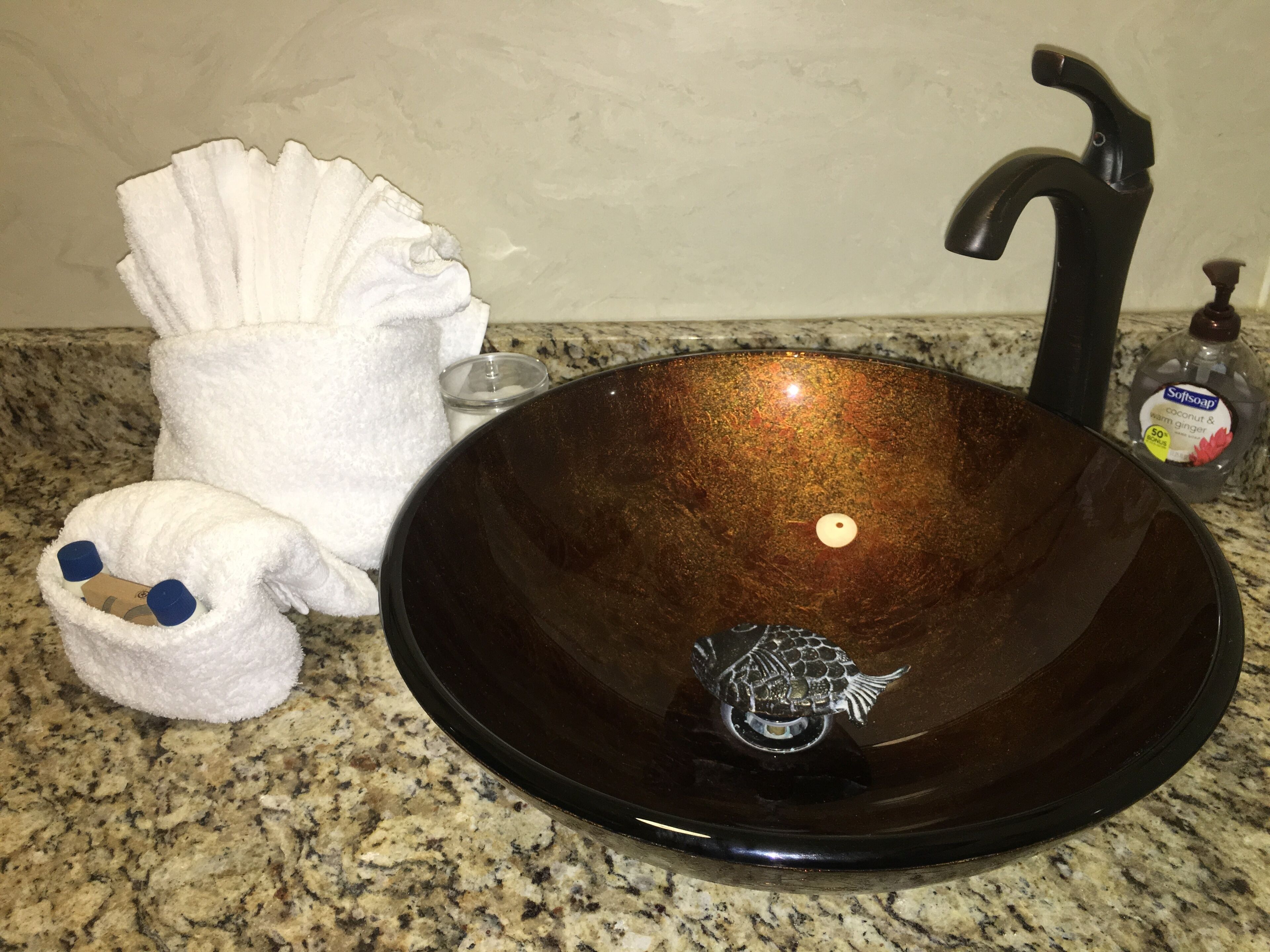 A kitchen sink with a brown basin, a white towel, a soap dispenser, and a small candle.