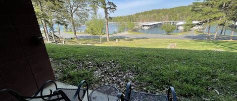 Un patio con dos sillas de metal y una mesa, con vista a una zona verde con árboles y una masa de agua.