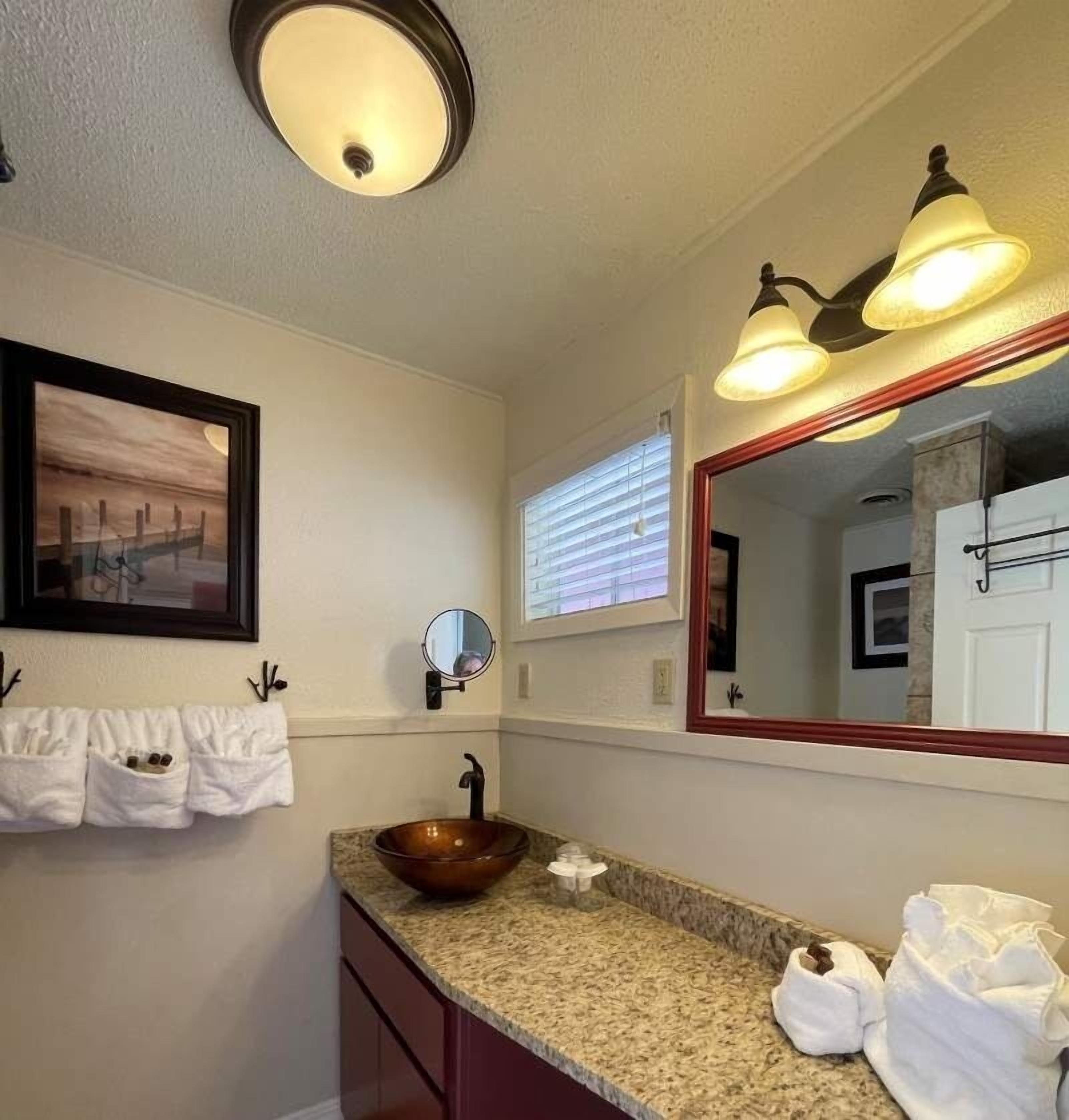 A bathroom with a large mirror, a sink with a copper basin, and a towel rack with towels.