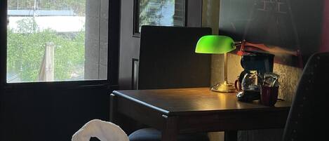 Ett hotellrum med en säng, ett skrivbord med en lampa, en stol, ett fönster med utsikt över träd och en tavla på väggen.