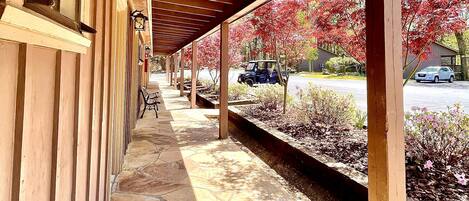A covered walkway with stone flooring, wooden beams, and a view of a parking area with red foliage.