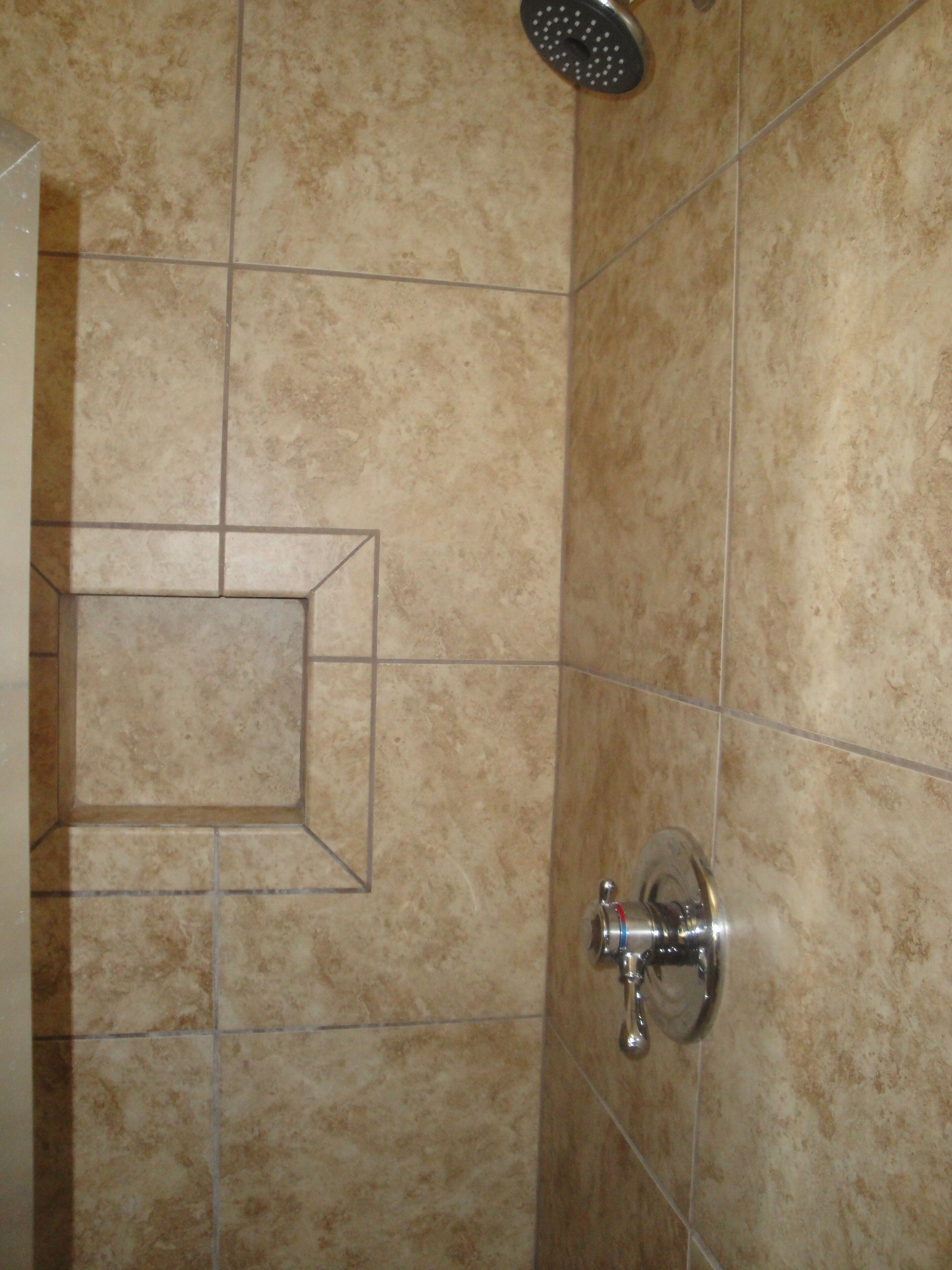 Une salle de bain avec des carreaux de couleur beige, une pomme de douche et un lavabo d’angle.