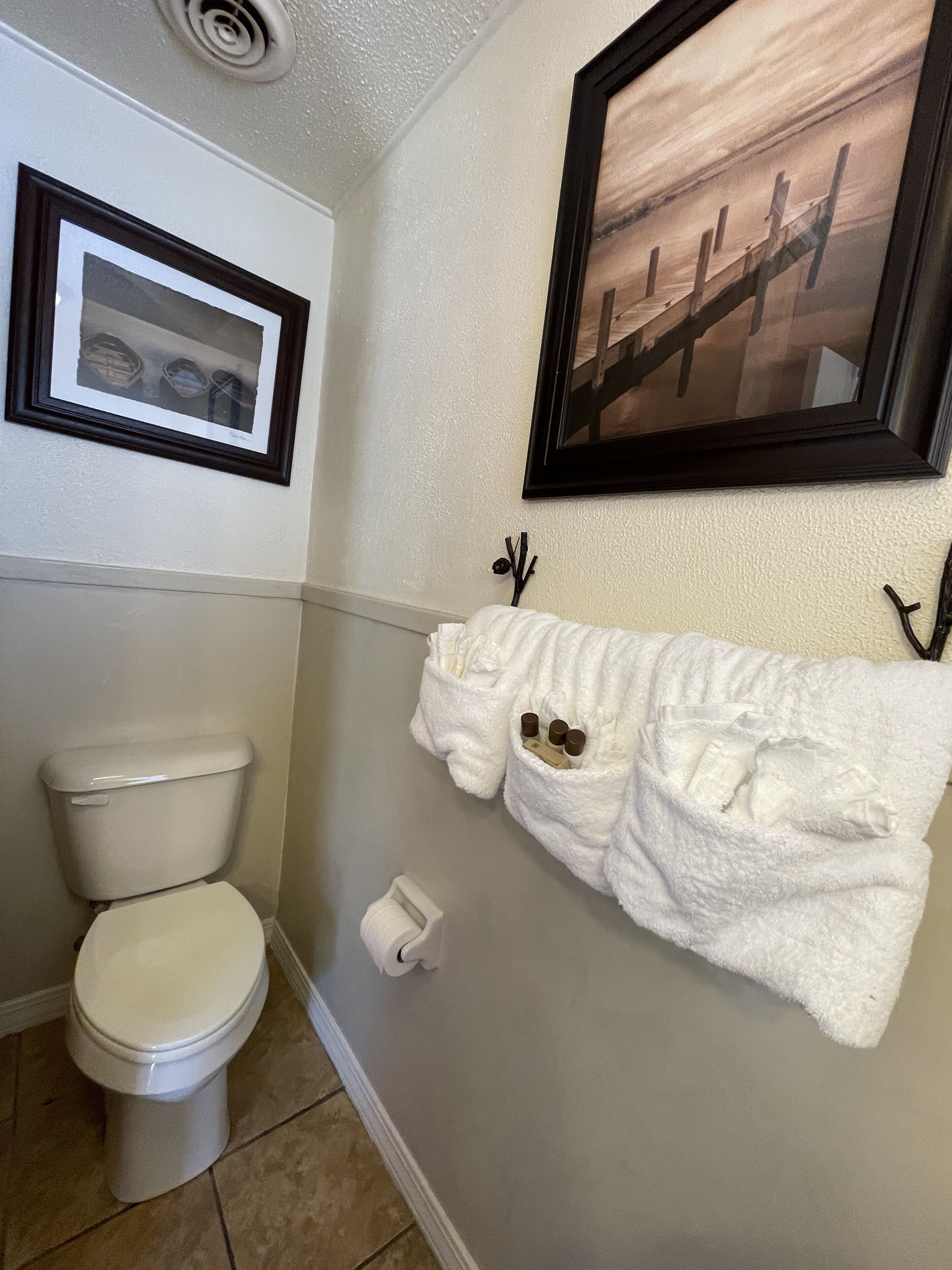 A bathroom with a toilet, a towel rack with a white towel, and two framed pictures on the wall.