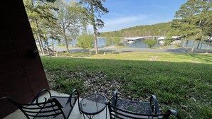A patio with two metal chairs and a table, overlooking a grassy area with trees and a body of water. - Mountain Harbor Queen Guest Room on Lake Ouachita by RedAwning (Mount Ida)