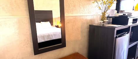 Hotellihuone, jossa on suuri peili, puinen penkki, pieni pöytä maljakolla, televisio ja jääkaappi.